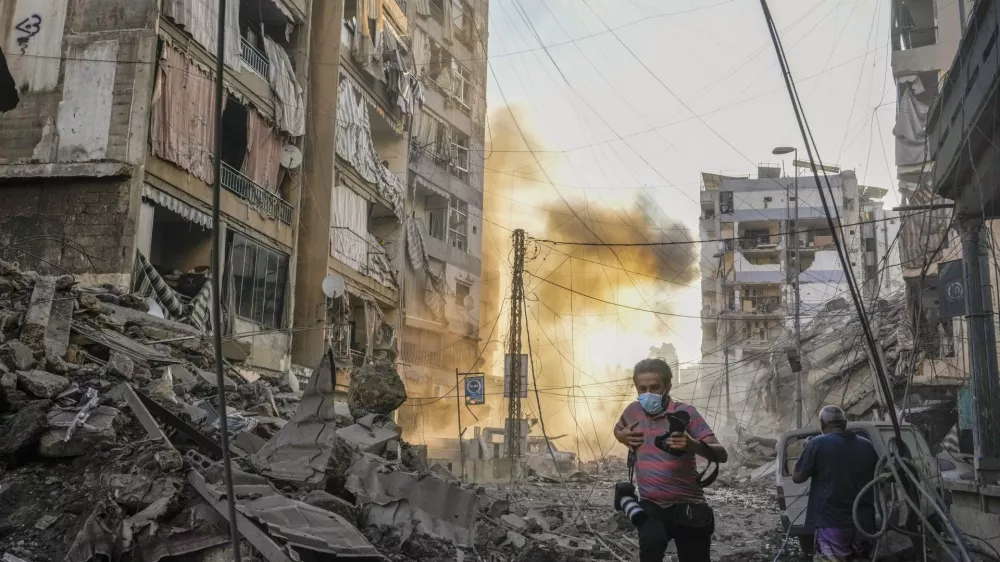 A photographer runs for cover as a smoke raises in the background following an Israeli airstrike in Dahiyeh, Beirut, Lebanon, Friday, Oct. 4, 2024. (AP Photo/Hassan Ammar)