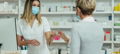 Female pharmacist wearing protective mask and serving a customer patient in a pharmacy and packing drugs in a paper bag