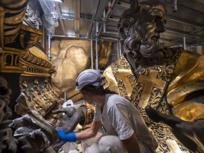 Restorer Eleonora Di Vittorio works, Tuesday, Oct. 8, 2024, in front of a bronze statue of St John Chrysostom, right, part of the Cathedra of St. Peter's inside St. Peter's Basilica at The Vatican where Bernini's monumental bronze canopy has been under restoration too since February by expert conservators who worked meticulously on its intricate surface. (AP Photo/Domenico Stinellis)