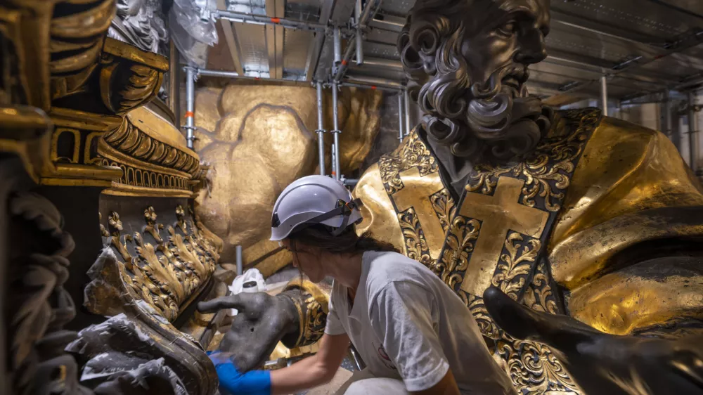 Restorer Eleonora Di Vittorio works, Tuesday, Oct. 8, 2024, in front of a bronze statue of St John Chrysostom, right, part of the Cathedra of St. Peter's inside St. Peter's Basilica at The Vatican where Bernini's monumental bronze canopy has been under restoration too since February by expert conservators who worked meticulously on its intricate surface. (AP Photo/Domenico Stinellis)