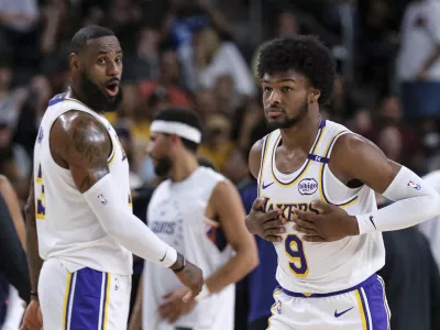 Los Angeles Lakers guard Bronny James (9), right, steps onto the court with Los Angeles Lakers forward LeBron James (23) during the first half of a preseason NBA basketball game Sunday, Oct. 6, 2024, in Palm Desert, Calif. (AP Photo/William Liang)