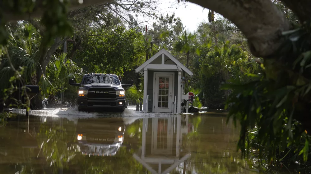 A pick up drives past a guard gate on a flooded street in Siesta Key, Fla., following the passage Hurricane Milton, Thursday, Oct. 10, 2024. (AP Photo/Rebecca Blackwell)