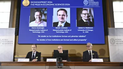 Academy of Sciences permanent secretary Hans Ellegren, center, Jakob Svensson, left, and Jan Teorell, of the Nobel assembly announce the Nobel memorial prize in economics winners, Daron Acemoglu, Simon Johnson and James A Robinson, seen on screen, during a press meeting at the Royal Swedish Academy of Sciences in Stockholm, Sweden, Monday Oct. 14, 2024. (Christine Olsson/TT News Agency via AP)