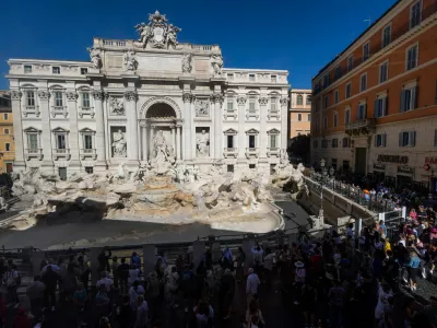 People stand in front of the Trevi Fountain, seen without water and surrounded by a fence as it undergoes extraordinary maintenance work ahead of the Jubilee 2025, in Rome, Italy, October 14, 2024. REUTERS/Guglielmo Mangiapane