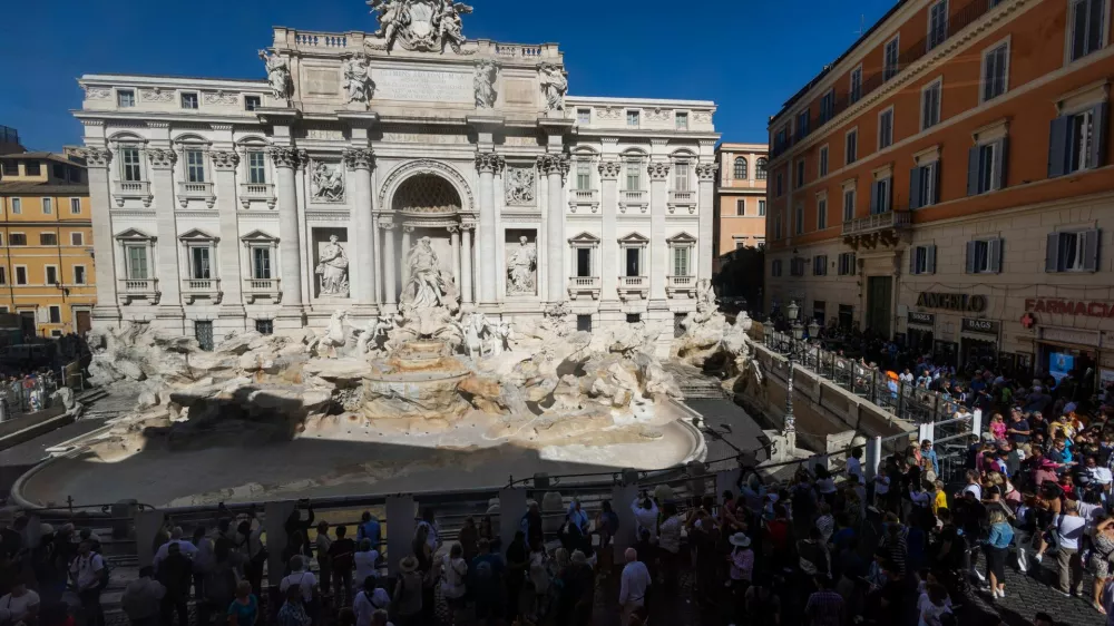 People stand in front of the Trevi Fountain, seen without water and surrounded by a fence as it undergoes extraordinary maintenance work ahead of the Jubilee 2025, in Rome, Italy, October 14, 2024. REUTERS/Guglielmo Mangiapane