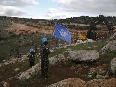 FILE - UN peacekeepers hold their flag, as they observe Israeli excavators attempt to destroy tunnels built by Hezbollah, near the southern Lebanese-Israeli border village of Mays al-Jabal, Lebanon, Dec. 13, 2019. (AP Photo/Hussein Malla, File)