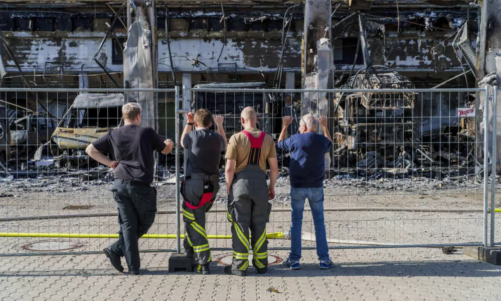 Firefighters stand at the fence and look at the burnt-out equipment, after the new equipment depot of the Stadtallendorf volunteer fire department burnt down with vehicles and equipment, causing millions in damage, in Stadtallendorf, Germany, Wednesday Oct. 16, 2024. (Andreas Arnold/dpa via AP)