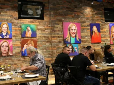 Customers eat a meal as portrait paintings by artist Helidon Haliti of Italy's Prime Minister Giorgia Meloni hang on the walls of "Trattoria Meloni" just outside a migrant processing camp set up by the Italian government, in Shengjin, Albania, October 15, 2024. REUTERS/Florion Goga