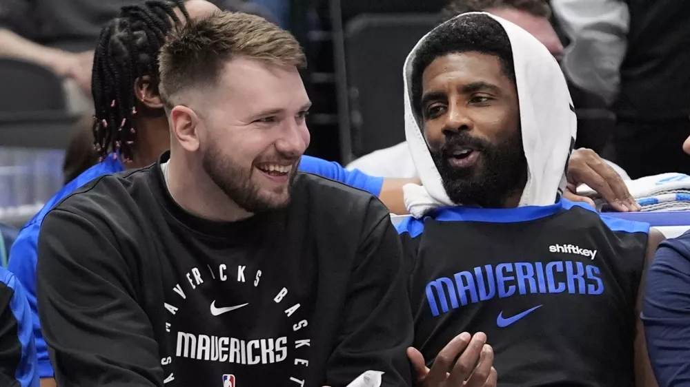 Sitting on the bench Dallas Mavericks guard Luka Doncic, left, shares a laugh with teammate fellow guard Kyrie Irving during a preseason NBA basketball game against the Milwaukee Bucks Thursday, Oct. 17, 2024, in Dallas. (AP Photo/LM Otero)