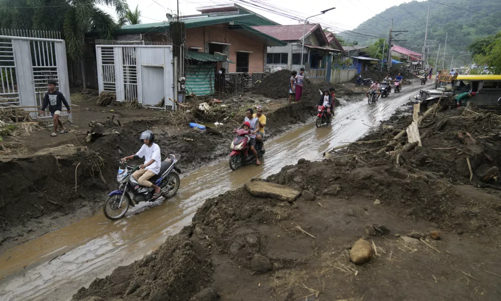 Residents ride motorcycles along a mud covered road after a landslide triggered by Tropical Storm Trami, recently struck Talisay, Batangas province, Philippines, Saturday, Oct. 26, 2024. (AP Photo/Aaron Favila)