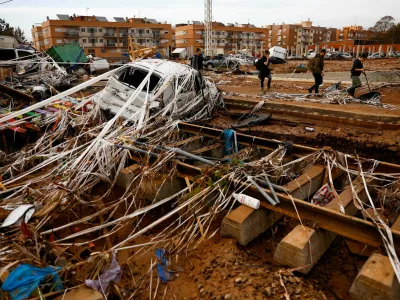 People walk past rail road tracks, damaged cars and debris after heavy rains in Alfafar, in Valencia, Spain, November 1, 2024. REUTERS/Susana Vera    TPX IMAGES OF THE DAY