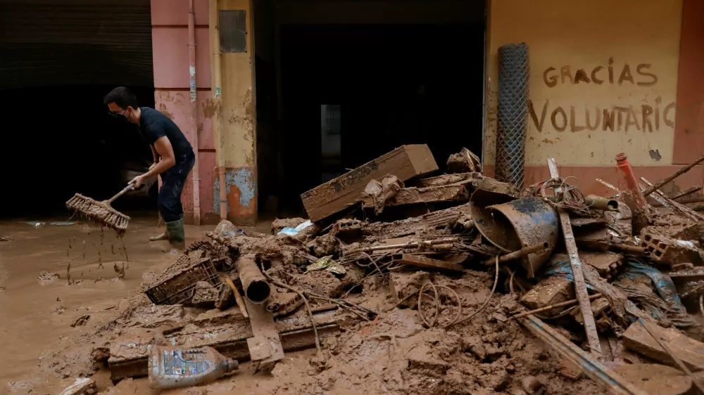 A man uses a broom next to mud-covered items and graffiti reading "Thank you volunteers", following heavy rains that caused floods, in Paiporta, near Valencia, Spain, November 3, 2024. REUTERS/Eva Manez