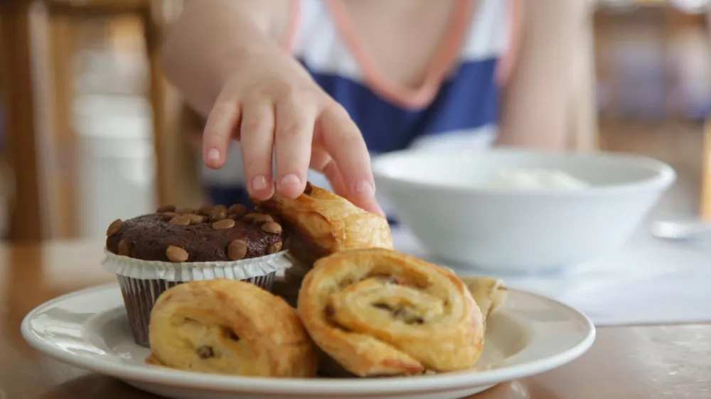 Close up of child's hand taking pastry from plate / Foto: Triocean