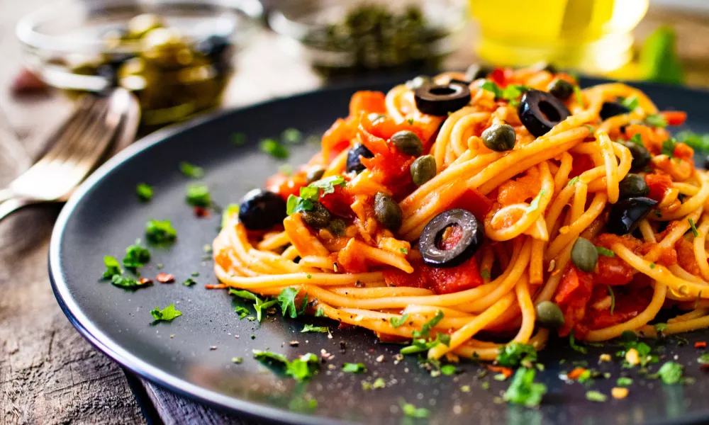 Pasta puttanesca with tomato sauce, anchovies, chilli, capers and olives on wooden table / Foto: Gbh007