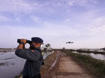 As the search for bodies continues, a Civil Guard looks though binoculars as a drone flies nearby at the mouth of the Poyo ravine in the La Albufera natural lake near Puerto de Catarroja, Valencia on the outskirts of Valencia, Spain, Tuesday, Nov. 5, 2024. (AP Photo/Alberto Saiz)