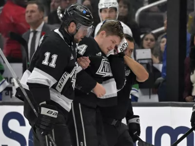 Los Angeles Kings defenseman Mikey Anderson, center, is helped off the ice by Los Angeles Kings center Anze Kopitar (11) after he was hit in the head with the puck during the second period of an NHL hockey game against the Vancouver Canucks, Thursday, Nov. 7, 2024, in Los Angeles. (AP Photo/Jayne-Kamin-Oncea)