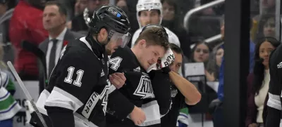 Los Angeles Kings defenseman Mikey Anderson, center, is helped off the ice by Los Angeles Kings center Anze Kopitar (11) after he was hit in the head with the puck during the second period of an NHL hockey game against the Vancouver Canucks, Thursday, Nov. 7, 2024, in Los Angeles. (AP Photo/Jayne-Kamin-Oncea)