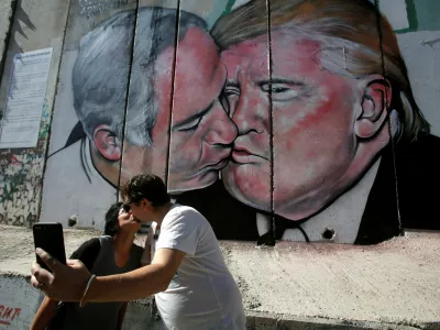 Tourists kiss each other as they stand in front of a mural depicting U.S. President Donald Trump and Israel's Prime Minister Benjamin Netanyahu kissing each other in the West Bank city of Bethlehem October 29, 2017. REUTERS/Mussa Qawasma NO RESALES. NO ARCHIVE.