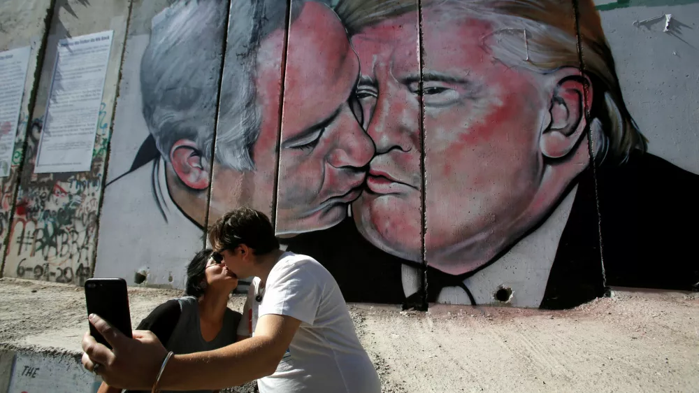 Tourists kiss each other as they stand in front of a mural depicting U.S. President Donald Trump and Israel's Prime Minister Benjamin Netanyahu kissing each other in the West Bank city of Bethlehem October 29, 2017. REUTERS/Mussa Qawasma NO RESALES. NO ARCHIVE.