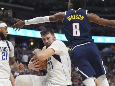 Dallas Mavericks guard Luka Doncic, center, pulls in a rebound as Denver Nuggets forward Peyton Watson defends in the second half of an NBA basketball game, Sunday, Nov. 10, 2024, in Denver. (AP Photo/David Zalubowski)