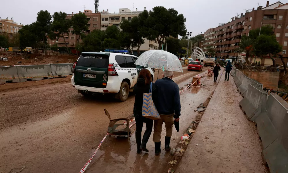 People with an umbrella cross a bridge covered with mud following catastrophic flooding, as Spain braces for torrential rain, in Paiporta, Valencia, November 13, 2024. REUTERS/Vincent West