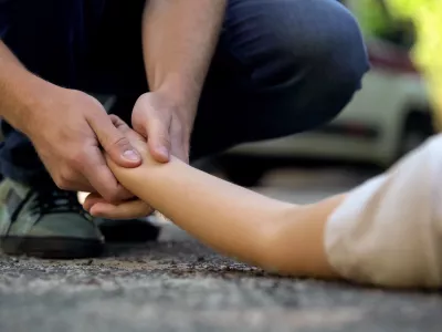 Man holding hand of girl lying on road, unconscious victim of car accident, 911 / Foto: Motortion