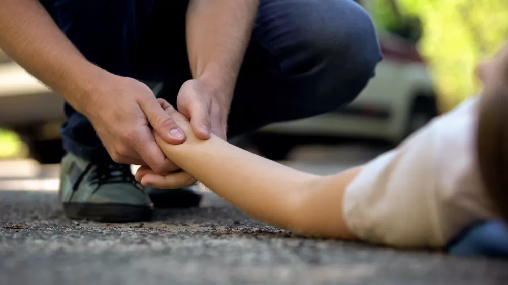 Man holding hand of girl lying on road, unconscious victim of car accident, 911 / Foto: Motortion