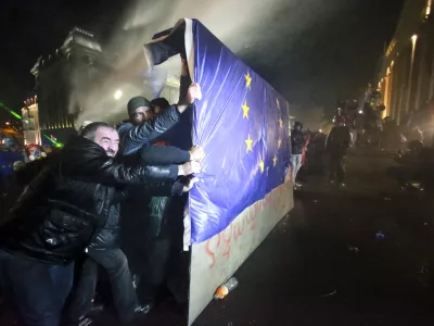 People hold a part of a fence with an EU flag as police use a water cannon to prevent protesters pouring into the streets following Georgian Prime Minister Irakli Kobakhidze's announcement, rallying outside the parliament building in Tbilisi, Georgia, Friday, Nov. 29, 2024. (AP Photo/Zurab Tsertsvadze)