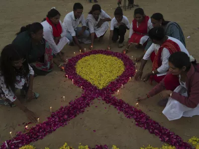 Members of a Non Government Organization(NGO) place candles around a symbol of 'red ribbon', the universal symbol of awareness and support for those living with HIV, on the eve of World AIDS Day, in Ahmedabad, India, Saturday, Nov. 30, 2024. (AP Photo/Ajit Solanki)