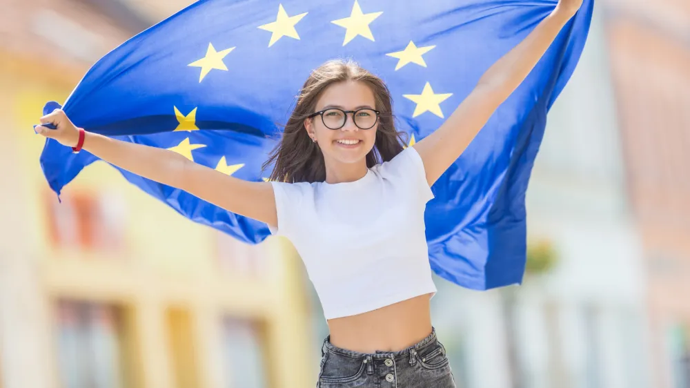 Cute happy young girl with the flag of the European Union in the streets somewhere in europe.