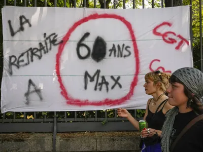 Women pass by a placard that reads: "Retirement age 60 maximum", during a protest in Paris, France, Tuesday, June 6, 2023. French unions are seeking to reignite resistance to President Emmanuel Macron's higher retirement age with what may be a final surge of nationwide protests and scattered strikes Tuesday. (AP Photo/Michel Euler)