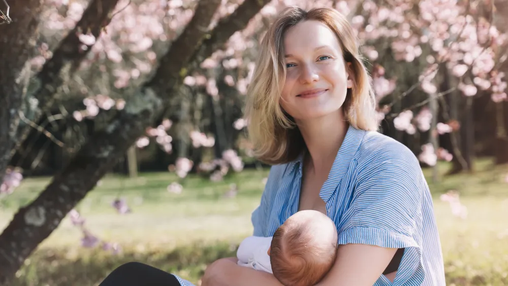 Beautiful mother breastfeeding baby. Young woman breast feeding her newborn baby. Concept of lactation infant, postpartum period, natural motherhood. Mother and baby on nature outdoors.