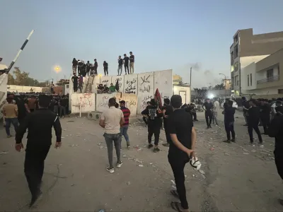 Protesters scale a wall at the Swedish Embassy in Baghdad Thursday, July 20, 2023. Protesters angered by the burning of a copy of the Quran stormed the embassy early Thursday, breaking into the compound and lighting a small fire. (AP Photo/Ali Jabar)