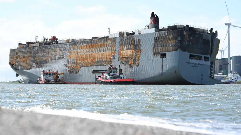 03 August 2023, Netherlands, Eemshaven: The badly damaged car carrier "Fremantle Highway" lies in the harbor. A good week after a fire broke out, the approximately 200-meter-long ship had been towed for hours to the North Sea port at the mouth of the Ems River. Photo: Lars Penning/dpa