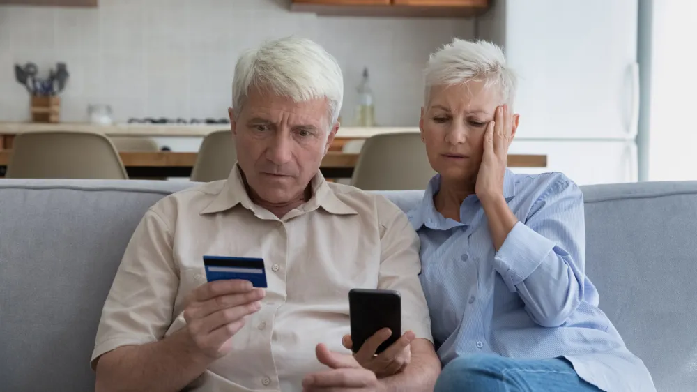 Shocked aged couple become victims of online fraud using credit card phone to pay for goods order service online on suspicious website. Frustrated older spouses overspending money at internet shopping