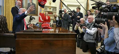 President Donald Trump throws a hat that reads "Trump Was Right About Everything" as he talks to reporters while Commerce Secretary Howard Lutnick, and White House press secretary Karoline Leavitt, back center, watch, in the Oval Office at the White House in Washington, Tuesday, Feb. 25, 2025. (Pool via AP)