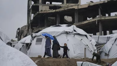 A Palestinian family walk between tents in a sprawling tent camp adjacent to destroyed homes and buildings in Gaza City, Gaza Strip, Saturday, March 1, 2025 during the Muslim holy month of Ramadan. (AP Photo/Abdel Kareem Hana)