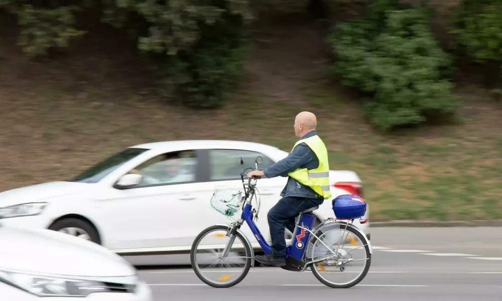 2FP3753 Belgrade, Serbia - May 14, 2021: One senior man wearing fluorescent vest riding an electric bike in city street traffic by the park