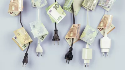 Electric power plugs with Euro banknotes on them hanging on light blue background. Energy efficiency, power consumption, electricity cost, and expensive energy concept. / Foto: Vejaa