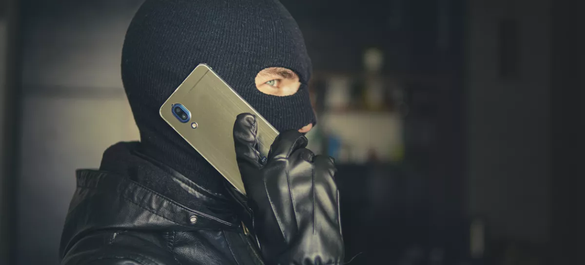 Young adult in black clothes with hidden face. Ill-intended fraudster uses mobile. Fraudster calls. Mobile racket. Hacker hijacks by phone. Cellphone account fraud. Scam / Foto: Diy13