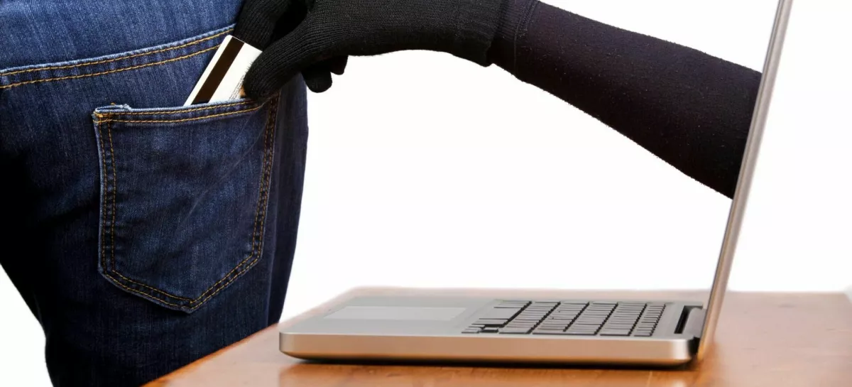 Internet theft - Concept: a gloved hand reaching through a laptop screen to steal a wallet from a man's pocket. / Foto: Davidevison